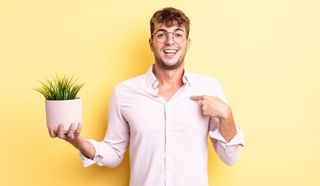 Jonge knappe man voelt zich gelukkig en wijst naar zichzelf met een opgewonden decoratief plantenconcept