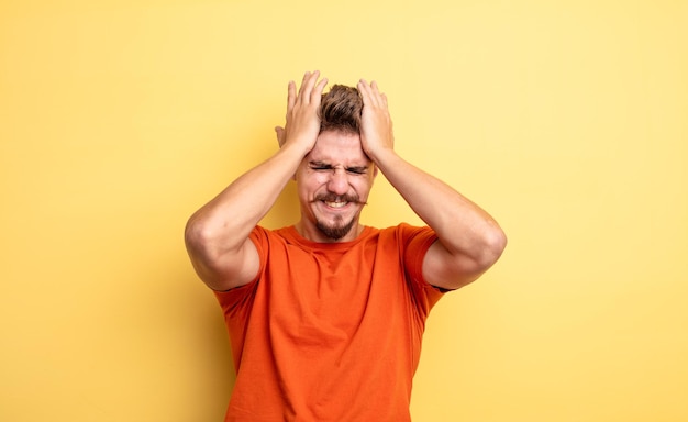 Jonge knappe man voelt zich gestrest en angstig, depressief en gefrustreerd met hoofdpijn, beide handen opstekend. vreemd snorconcept