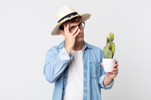 Jonge knappe man voelt zich verveeld, gefrustreerd en slaperig na een vermoeiende. boer met een decoratieve cactus