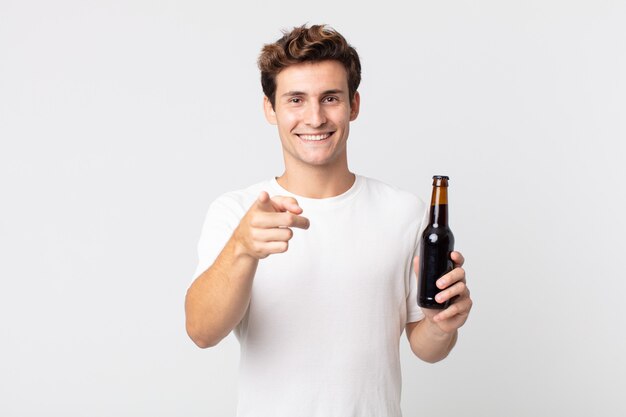 Jonge knappe man wijzend op de camera die jou kiest en een bierfles vasthoudt