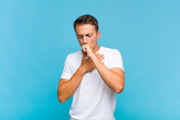 Jonge knappe man ziek met keelpijn en griepsymptomen, hoesten met bedekte mond