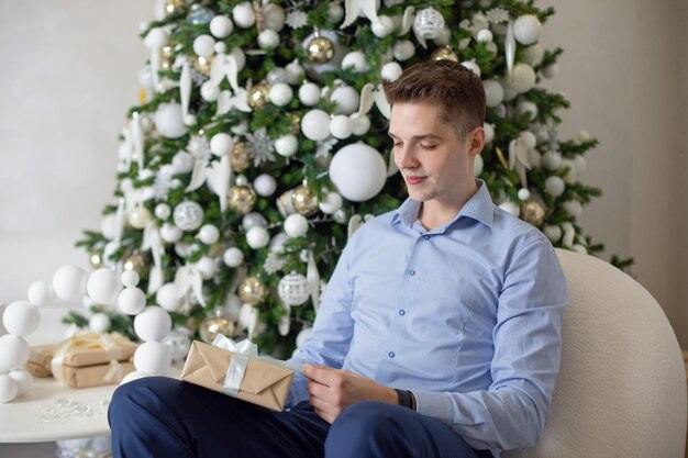 Jonge knappe man zit in de woonkamer en houdt een kerstcadeau vast.