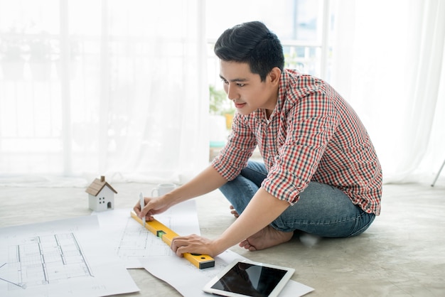 Jonge knappe mannelijke aziatische architect die thuis op de vloer werkt.