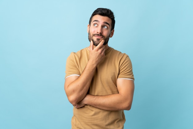 Jonge knappe mens die met baard over geïsoleerde muur een idee denken terwijl omhoog het kijken