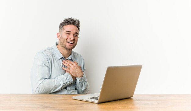 Jonge knappe mens die met zijn laptop werken die houdend handen aan hart, concept lachen lachen.