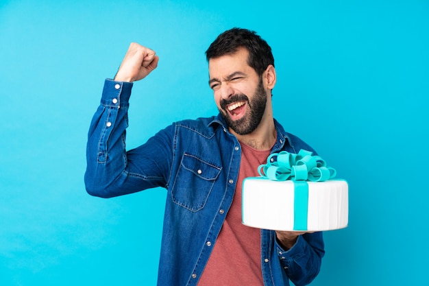 Jonge knappe mens met een grote cake over geïsoleerd blauw