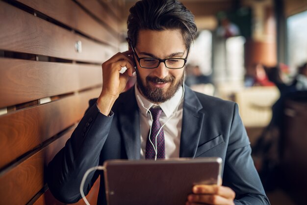 Jonge knappe moderne zakenman die een onderbreking nemen bij koffiewinkel en een tablet gebruiken.