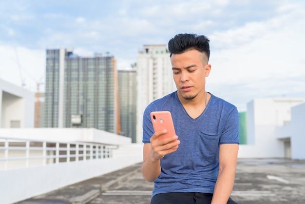 Jonge knappe multi-etnische man zitten en met behulp van telefoon tegen uitzicht over de stad