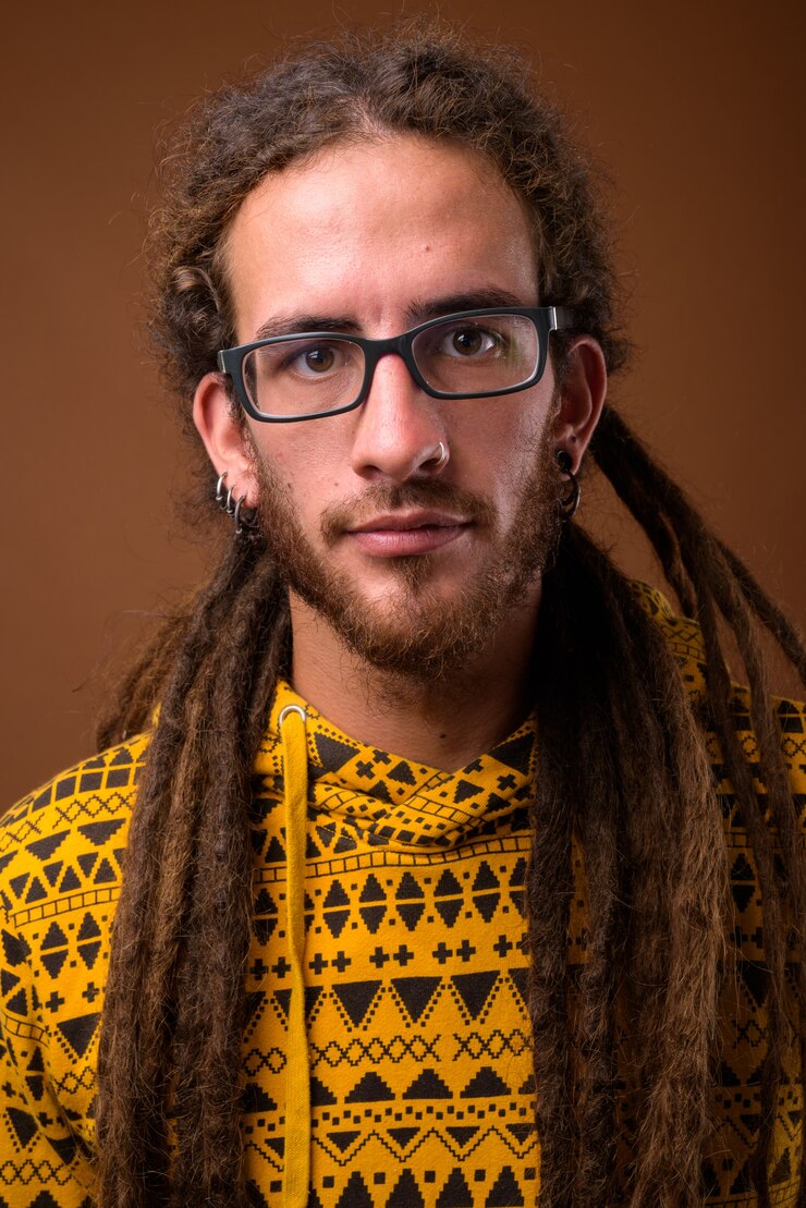 Foto jonge knappe spaanse man met dreadlocks tegen bruine achtergrond