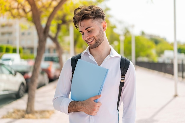 Jonge knappe studentenmens in openlucht met gelukkige uitdrukking