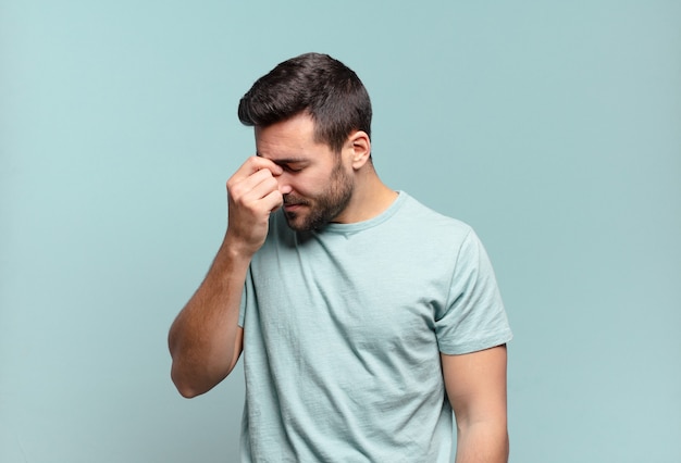 Jonge knappe volwassen man die zich gestrest, ongelukkig en gefrustreerd voelt, het voorhoofd aanraakt en lijdt aan migraine of ernstige hoofdpijn