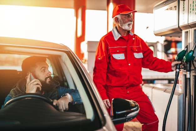 Jonge knappe volwassen man en senior werknemer bij tankstation en tanken auto.