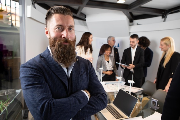 Foto jonge knappe zakenman glimlachend in een kantoor geposeerd portret met selectieve focus op de zakenman en collega's wazig op de achtergrond