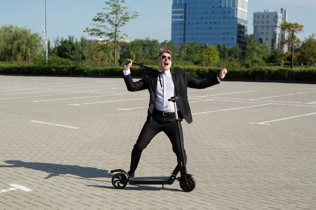 Jonge knappe zakenman in een pak rijdt een elektrische scooter door de stad en lacht