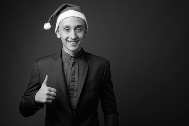 jonge knappe zakenman met kerstmuts klaar voor Kerstmis tegen grijze muur. zwart en wit