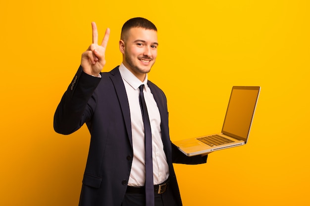 Jonge knappe zakenman tegen vlakke achtergrond die laptop houdt