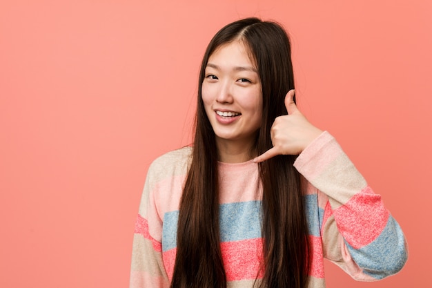 Jonge koele Chinese vrouw die een mobiel telefoongesprekgebaar met vingers toont.