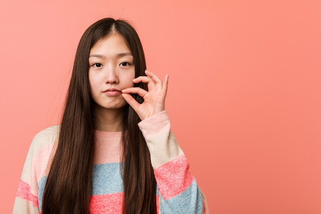 Jonge koele Chinese vrouw met vingers op lippen die een geheim houden.