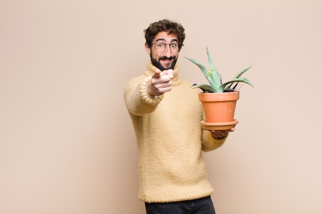 Jonge koele mens die een cactusinstallatie houden tegen vlakke muur