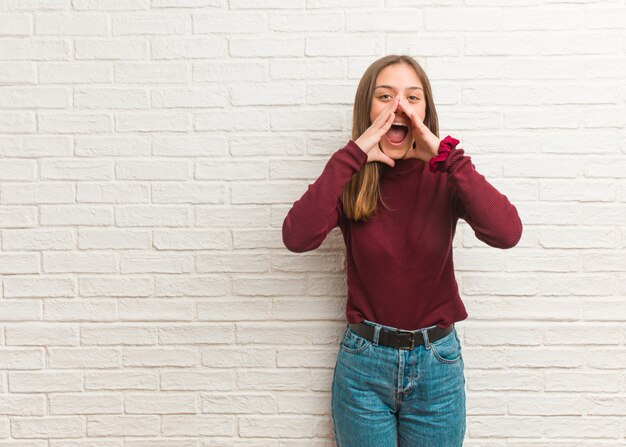 Jonge koele vrouw over een bakstenen muur die iets gelukkig aan de voorzijde schreeuwt