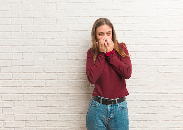 Jonge koele vrouw over een bakstenen muur die om iets lacht, die mond met handen behandelt