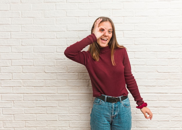 Jonge koele vrouw over een zekere bakstenen muur zeker doend ok gebaar op oog