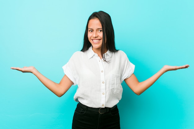 Jonge koele vrouw tegen een blauwe muur die een welkome uitdrukking toont