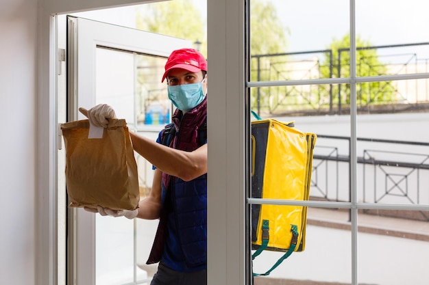 Jonge koerier met thermotas bij de ingang naar huis. Maaltijdbezorgservice