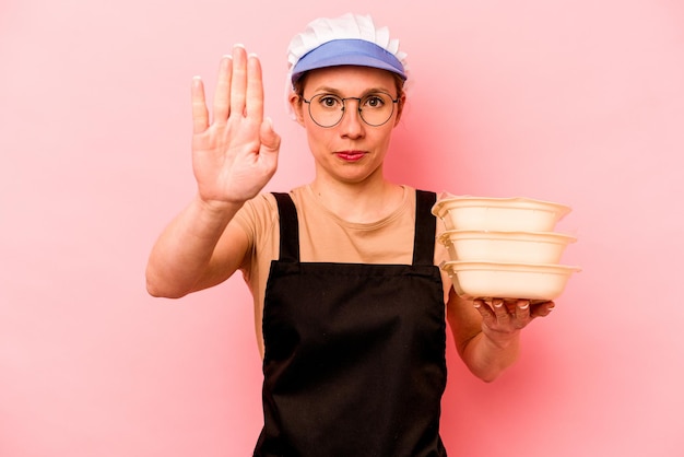 Jonge kok vrijwilligersvrouw geïsoleerd op een roze achtergrond die staat met uitgestrekte hand met stopbord dat je verhindert
