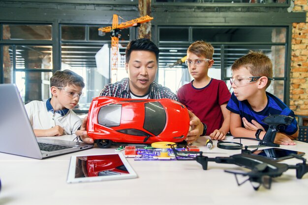 Jonge koreaanse man van elektronica-ingenieur met jonge kinderen met behulp van schroevendraaier te demonteren robotmachine aan de tafel in de moderne school. slow motion