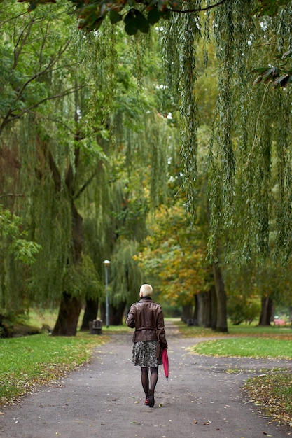 Foto jonge kortharige blonde vrouw loopt in het herfstpark met rode paraplu uitzicht vanaf de achterkant