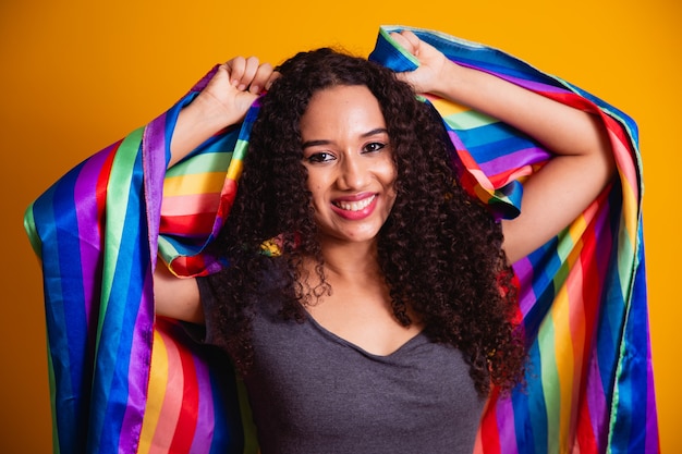 Jonge krullende haarvrouw die met de vlag van de lgbttrots behandelen. alleen. een. vuist omhoog houden, lgbt-vlag bedekken. lgbt+ vlag op gele achtergrond.