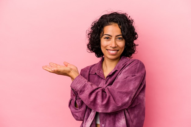 Jonge krullende Latijns-vrouw geïsoleerd op roze achtergrond met een kopie ruimte op een palm.