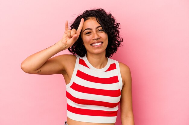 Jonge krullende Latijns-vrouw geïsoleerd op roze achtergrond met rock gebaar met vingers