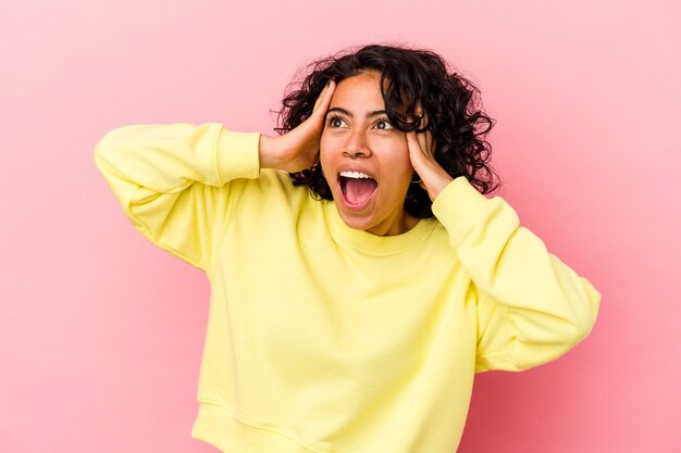 Jonge krullende Latijns-vrouw geïsoleerd op roze achtergrond schreeuwen, erg opgewonden, gepassioneerd, tevreden met iets.