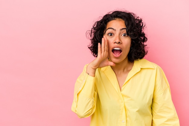 Jonge krullende Latijns-vrouw geïsoleerd op roze achtergrond schreeuwt luid, houdt ogen geopend en handen gespannen.