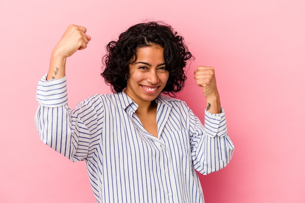 Jonge krullende Latijns-vrouw geïsoleerd op roze achtergrond zorgeloos en opgewonden juichen. Overwinningsconcept.