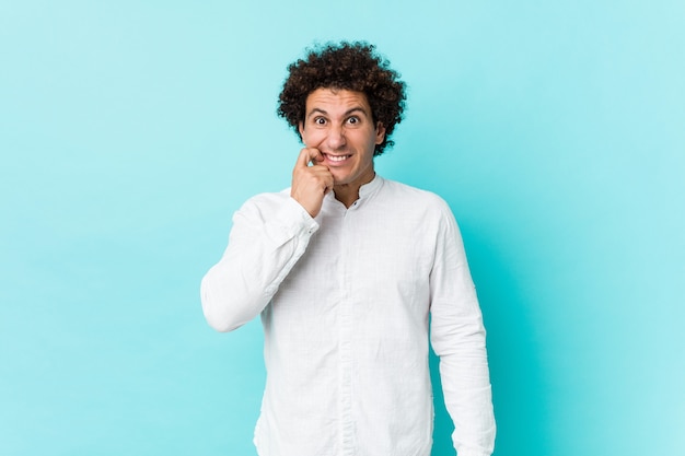 Jonge krullende volwassen man draagt een elegant shirt bijt nagels, nerveus en erg angstig.