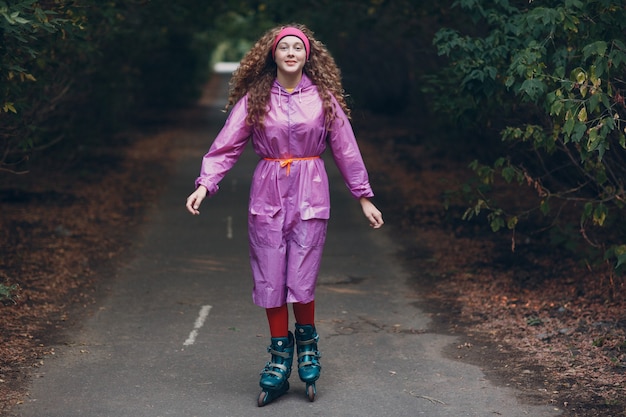 Jonge krullende vrouw die rolschaatsen gaat in het park.