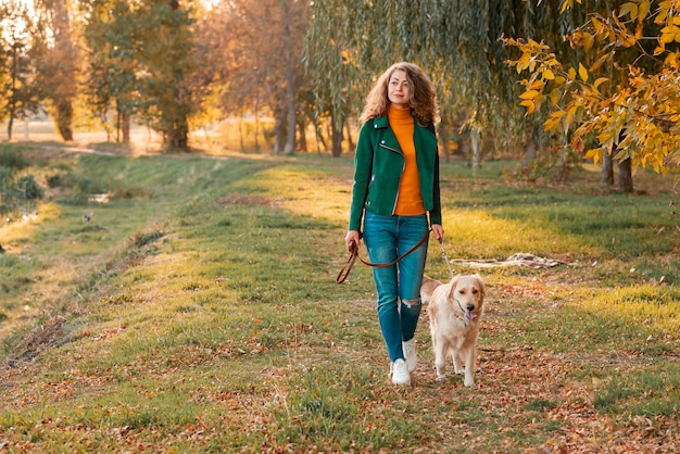 Jonge krullende vrouw met haar hond in de herfstbladeren