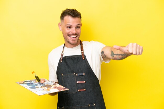 Jonge kunstenaar blanke man met een palet geïsoleerd op gele achtergrond met een duim omhoog gebaar