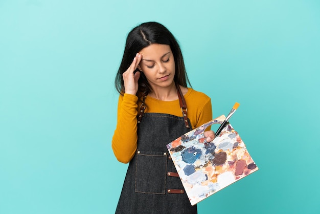 Jonge kunstenaar blanke vrouw met een palet geïsoleerd op blauwe achtergrond met hoofdpijn