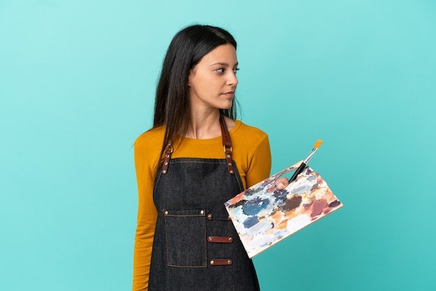 Jonge kunstenaar blanke vrouw met een palet geïsoleerd op blauwe achtergrond op zoek naar de zijkant