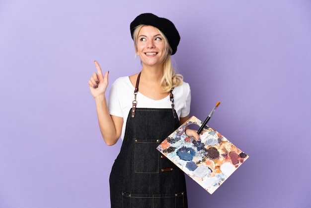 Jonge kunstenaar Russische vrouw met een palet geïsoleerd op een paarse achtergrond die een geweldig idee naar boven wijst