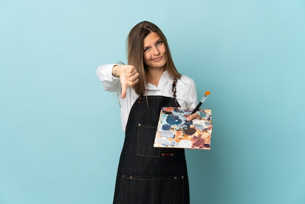 Jonge kunstenaars Slowaakse vrouw die op blauwe muur wordt geïsoleerd die duim neer met negatieve uitdrukking toont