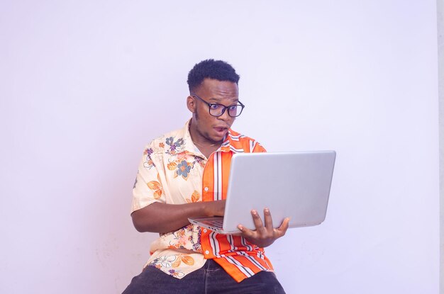 Jonge lachende Afro-Amerikaanse man permanent en met behulp van laptopcomputer geïsoleerd op witte achtergrond