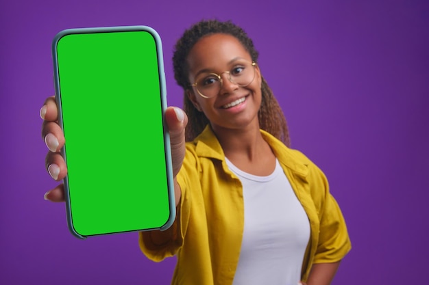 Jonge lachende afro-amerikaanse studente toont telefoon met groen scherm