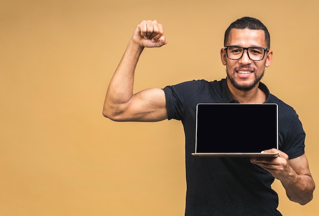 Jonge lachende Afro-Amerikaanse zwarte man permanent en met behulp van laptopcomputer geïsoleerd op beige achtergrond PC-scherm weergegeven: