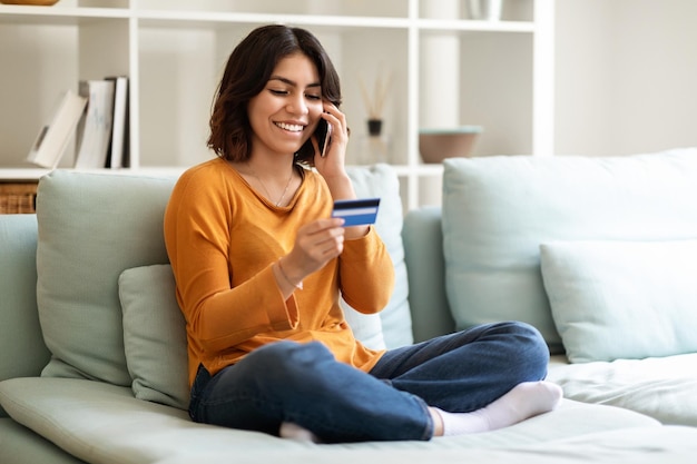 Jonge lachende Arabische vrouw met creditcard en praten op mobiele telefoon