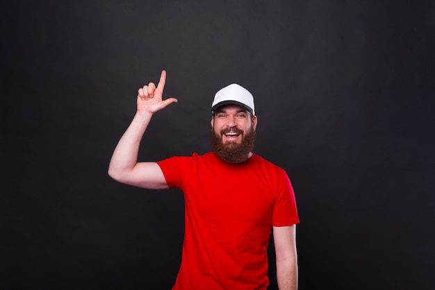 jonge lachende bebaarde man in rood t-shirt die omhoog wijst op copyspace